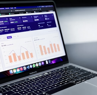 A laptop with an open screen displaying dashboard analytics featuring charts, graphs, and numerical data related to sales and subscriptions. The interface is predominantly dark-themed with sections highlighting key performance metrics. The device shown is a MacBook Pro, indicated by the keyboard layout and branding.