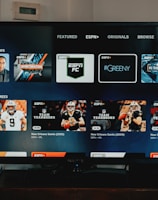 A television screen displaying the ESPN+ streaming interface with various sports-related shows and categories. The screen includes sections such as 'Browse by Shows' and 'Best of Drew Brees' with thumbnails of sports programs featuring athletes in action and analysts.